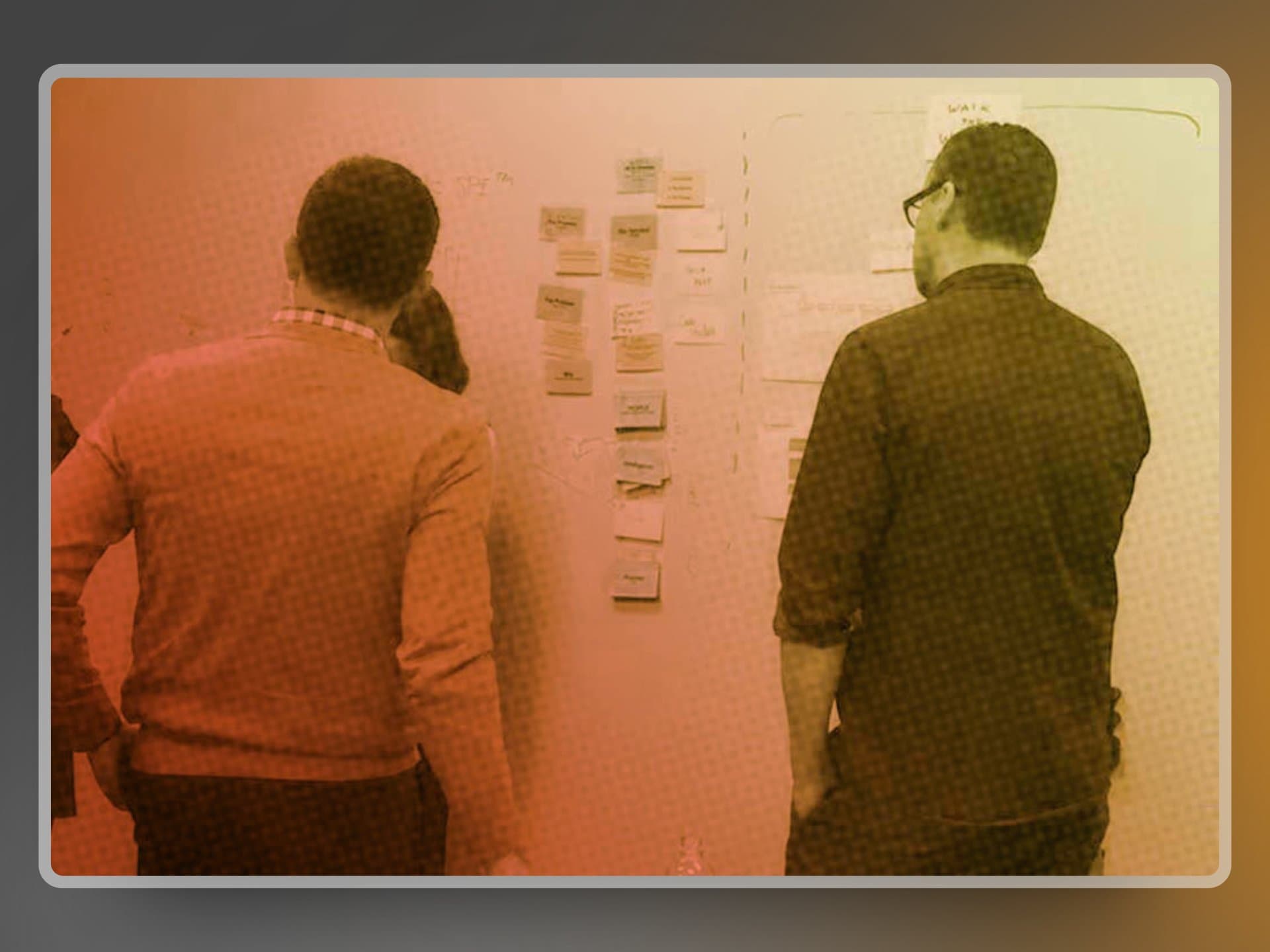 Two team members synthesizing field research notes on a whiteboard with sticky-note clusters